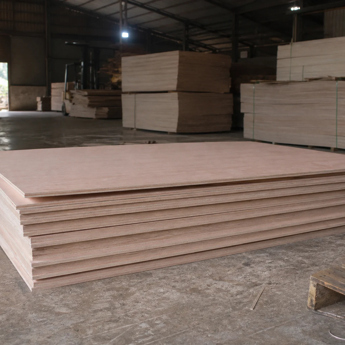 Stack of Okoume-faced plywood on a mill floor, smooth pale pinkish-tan face